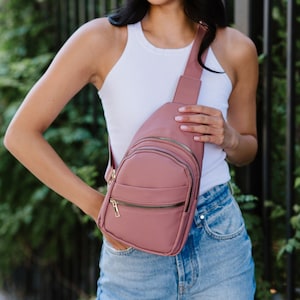 A woman wearing a mauve sling crossbody bag.