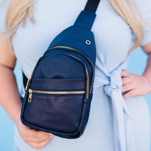 A woman wearing a navy sling crossbody bag.