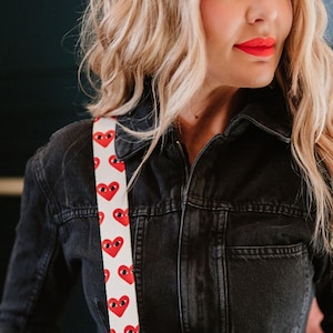 A woman wearing a white bag strap with red hearts with eyes.