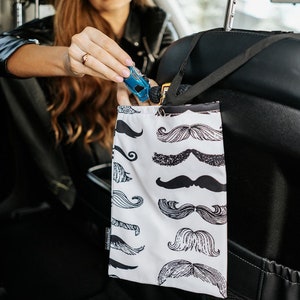 May include: A white car seat organiser with a black strap and a black and white pattern of moustaches. The organiser is hanging on the back of a car seat.