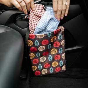 May include: A brown fabric car trash can with a colourful pattern of trees and circles. The trash can is hanging on the back of a car seat.