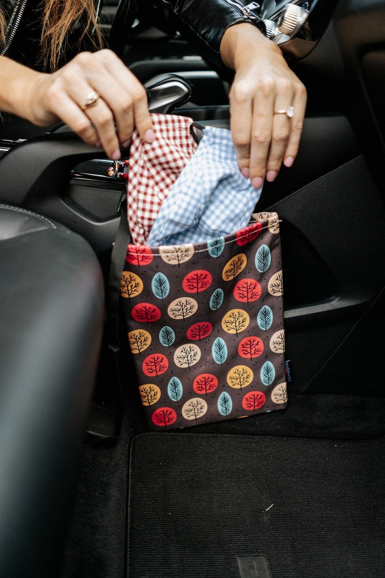 May include: A brown fabric car trash can with a colourful pattern of trees and circles. The trash can is hanging on the back of a car seat.