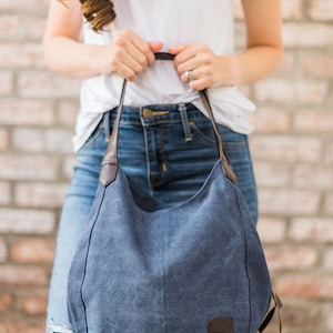 A woman holding a navy blue hobo bag. The bag is made from canvas and the handles are vegan leather.