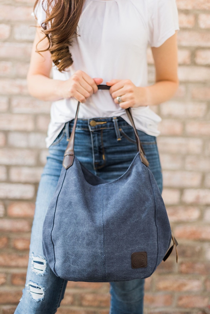 A woman holding a navy blue hobo bag. The bag is made from canvas and the handles are vegan leather.