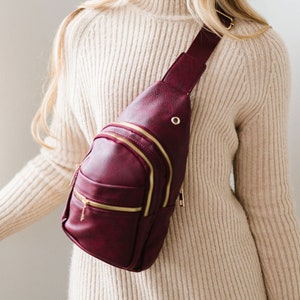 A woman wearing a burgundy sling crossbody bag.