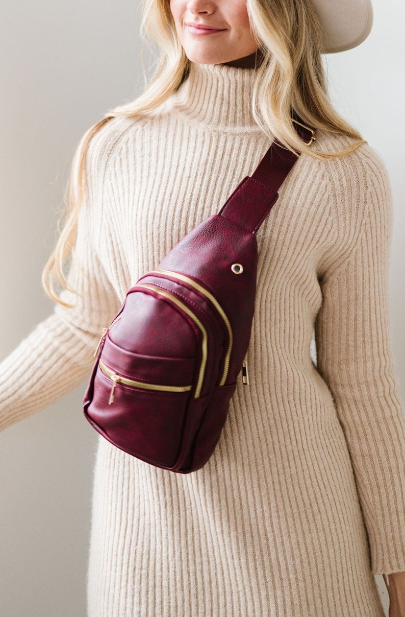 A woman wearing a burgundy sling crossbody bag.