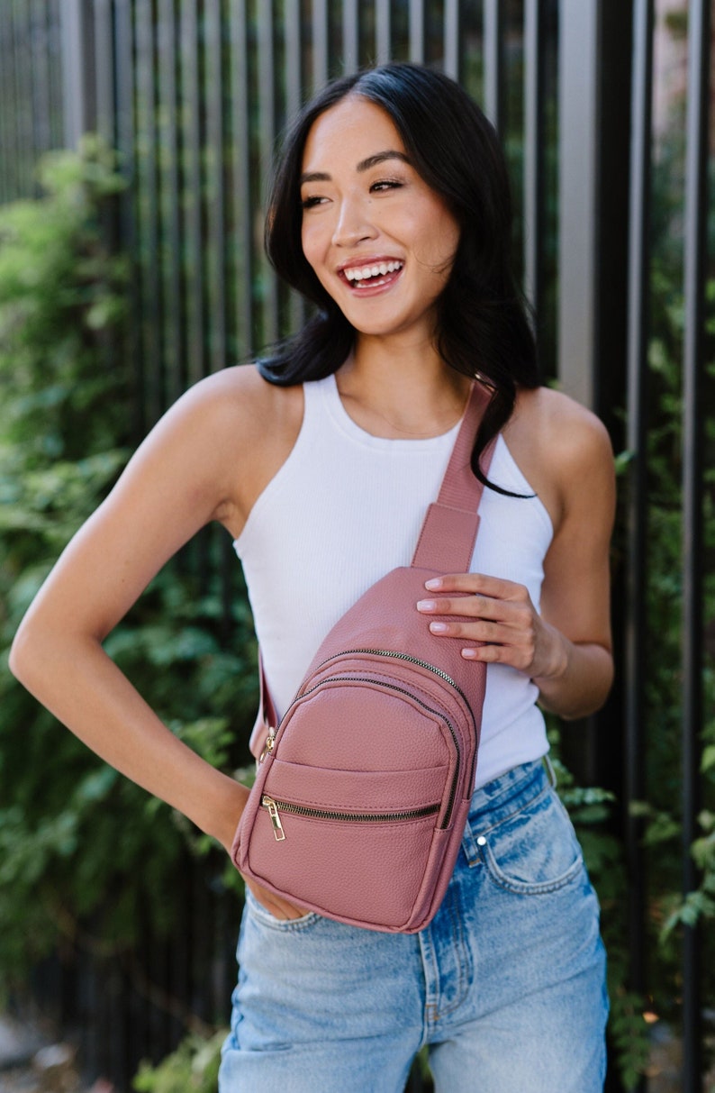 A woman wearing a mauve sling crossbody bag.