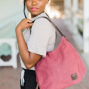 A woman wearing maroon canvas hobo bag on her shoulder.