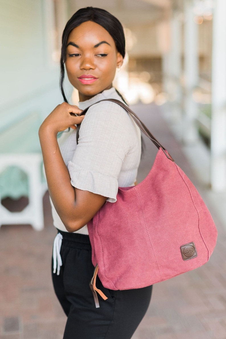 A woman wearing maroon canvas hobo bag on her shoulder.