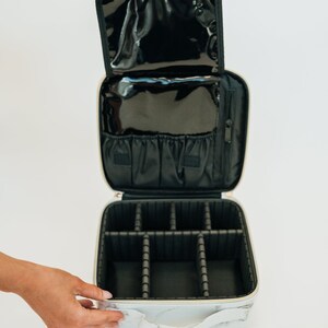 May include: White and gray marble-patterned makeup bag with a black interior. The bag has a zipper closure and a handle. The interior has multiple compartments for organizing makeup and other items.