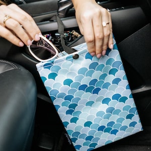 May include: A blue and white patterned car trash bag with a snap closure. The bag is hanging from a headrest in a car.