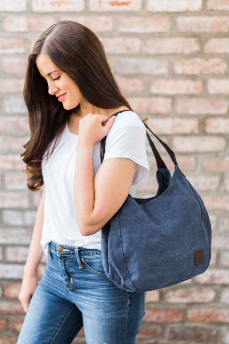 A woman wearing navy canvas hobo bag on her shoulder.