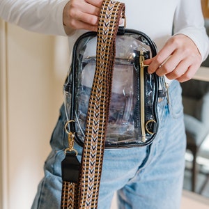 A woman holds a black clear sling bag with a back zippered pocket.