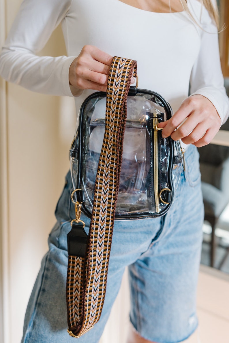 A woman holds a black clear sling bag with a back zippered pocket.