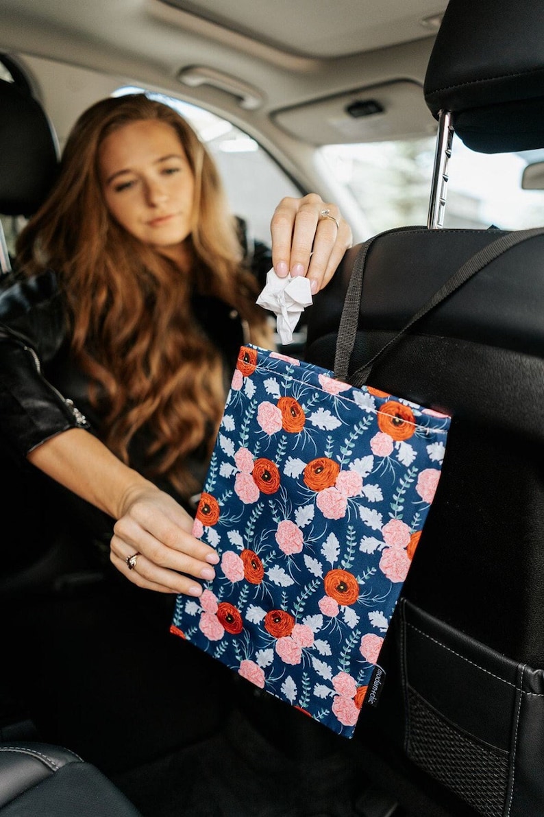 May include: A floral patterned car trash bag hanging from the backseat headrest. The bag is blue with red and pink flowers and green leaves. The bag is labelled "audible"