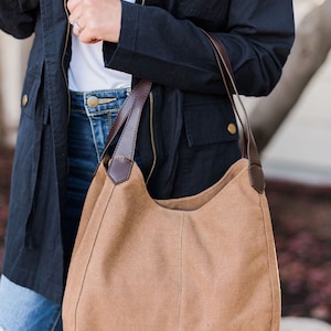 A woman wearing a brown hobo style bag on her arm. The bag is made from canvas and the handles are vegan leather.