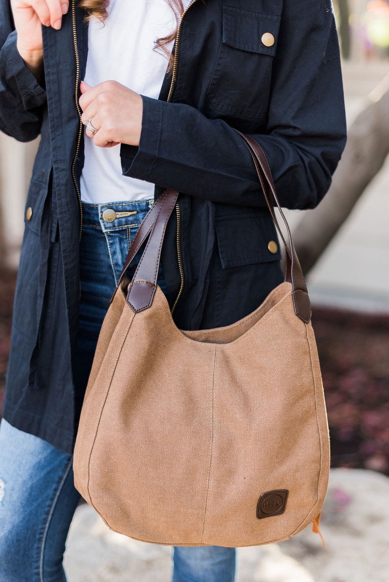 A woman wearing a brown hobo style bag on her arm. The bag is made from canvas and the handles are vegan leather.