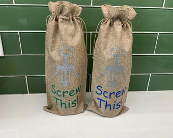 May include: Two brown burlap wine bottle bags with a silver corkscrew design and the text "Screw This!" in green and blue lettering.
