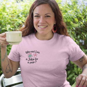 May include: A light pink t-shirt with the text "Why can't I use a Joker for a pair?" and illustrations of a joker and a mahjong tile. The shirt is being worn by a person holding a beige mug.