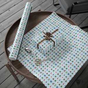 Wrapped package, and wrapping paper. the paper has white Mahjong tiles on a light blue background. The package has a string bow. Also on the table are a pair of scissors and greenery.