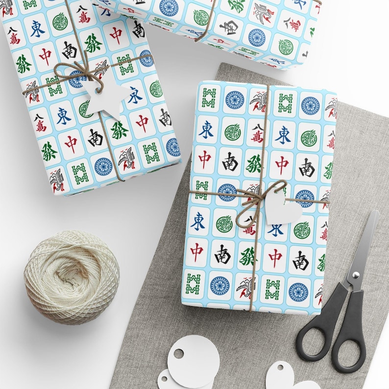 Close up of package, wrapped in paper with white Mahjong tiles on a light blue background. It is decorated with a twine bow.