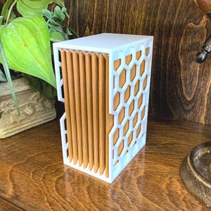 May include: White and brown geometric storage box with a honeycomb pattern on the front and sides. The box is made of wood and has a white finish.