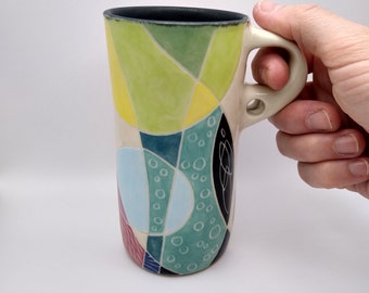 Handbuilt tall porcelain tumbler with one-fingered handle, underglaze painting and sgraffito, abstract colorful design with multiple glazes