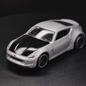 May include: A silver toy car with a black bonnet, black wheels, and a black interior. The car is a sports car with a low profile and a sleek design.
