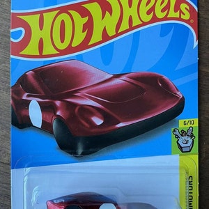May include: A red Hot Wheels Coupe Clip toy car with a white stripe on the side. The car is on a blue background with the Hot Wheels logo and the words "Experimotors" and "6/10".