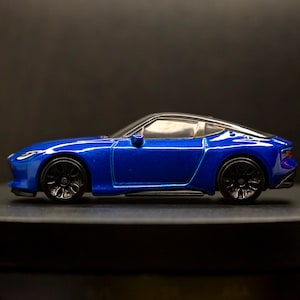 May include: A blue toy car model with black wheels and a black interior. The car is a coupe with a sleek design.