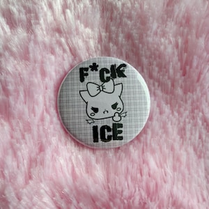 May include: A round button with a cartoon character design. The button features a black and white illustration of a cat-like creature with a bow and the text "F*CK ICE". The background has a plaid pattern.