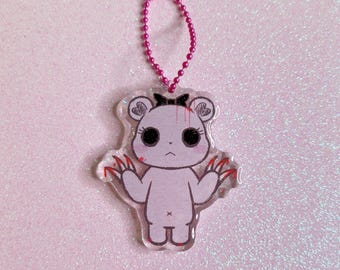 May include: A pink bear charm with a pink bow and red claws. The bear has a bloody face and is made of clear acrylic.