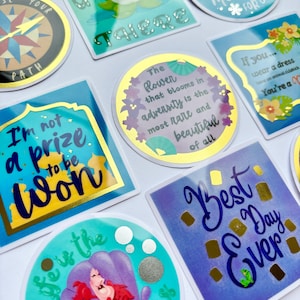 Könnte beinhalten: Eine Sammlung farbenfroher Aufkleber mit verschiedenen Designs und Zitaten. Die Aufkleber haben goldfarbene Akzente und enthalten Sätze wie "Best Day Ever", "I'm not a prize to be won" und "Life is the bubbles". Die Aufkleber sind in verschiedenen Formen.