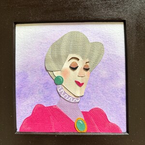 Puede incluir: Retrato enmarcado en papel de una mujer con cabello gris, vestida con un vestido rosa y aretes verdes. El fondo es un lavado de acuarela de color p&uacute;rpura y blanco. El marco es negro.