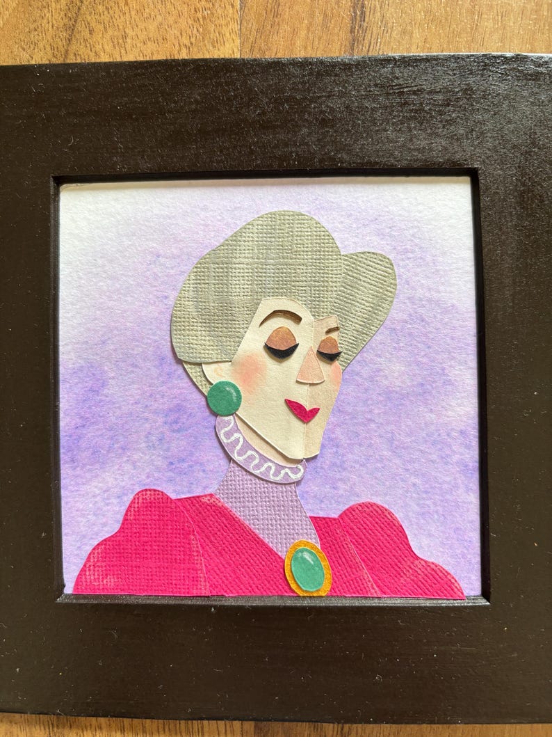 Puede incluir: Retrato enmarcado en papel de una mujer con cabello gris, vestida con un vestido rosa y aretes verdes. El fondo es un lavado de acuarela de color p&uacute;rpura y blanco. El marco es negro.