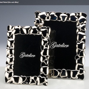 May include: Two silver picture frames with a heart design. The frames are made of a die-cast alloy and are nickel plated. The larger frame has the word "Gatelier" inscribed on the black mat.