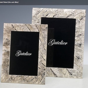 May include: Two silver-plated picture frames with a feather design. The frames are made of die-cast alloy and feature the word "Gatelier" on the front.
