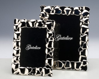 May include: Two silver picture frames with a heart design. The frames are made of a die-cast alloy and are nickel plated. The larger frame has the word "Gatelier" inscribed on the black mat.