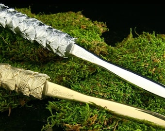 May include: Two letter openers with ginkgo leaf designs. The top opener is silver and the bottom opener is gold. Both openers have the word "Calcior" engraved on the blade.