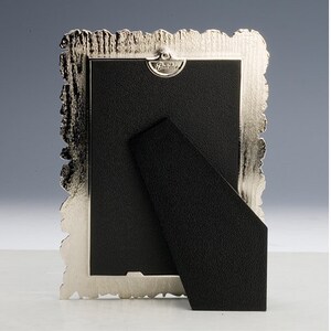 May include: Silver-toned picture frame with an ornate, textured border. The frame has a black backing and a kickstand.