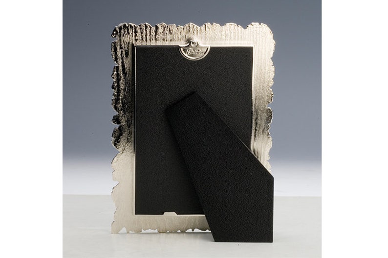 May include: Silver-toned picture frame with an ornate, textured border. The frame has a black backing and a kickstand.