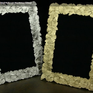 May include: Two 4x6 inch picture frames made of bronze casting. The frames are decorated with a ginkgo leaf design. One frame is titanium gold and the other is silver.
