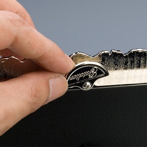 May include: A silver-toned picture frame with a decorative, scalloped edge. The frame has a black backing and a small, silver-toned latch with the word "Barclay" engraved on it.