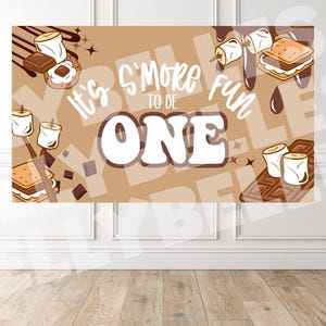 May include: A banner with a brown background and the text "It's S'more Fun to be ONE". The banner features illustrations of s'mores, chocolate, and marshmallows. The banner is designed for a first birthday celebration.