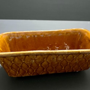 May include: A brown ceramic rectangular planter with a woven pattern. The planter has a glazed finish and is ideal for displaying small plants or succulents.