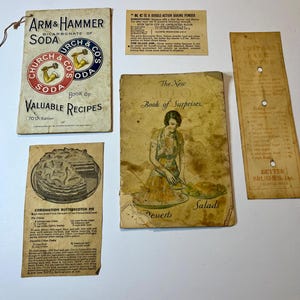 May include: A collection of vintage recipe cards and booklets. Includes an "Arm & Hammer Soda" booklet, a "KC is a Double-Action Baking Powder" card, a "Sanitary Cake Tester" card, and a "Book of Surprises" booklet with desserts and salads.