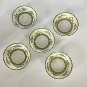May include: Set of five white ceramic bowls with green and gold floral designs. The bowls have a white interior and a slightly raised rim.