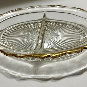 May include: A clear glass divided serving dish with a gold rim. The dish has a scalloped edge and a raised center divider.