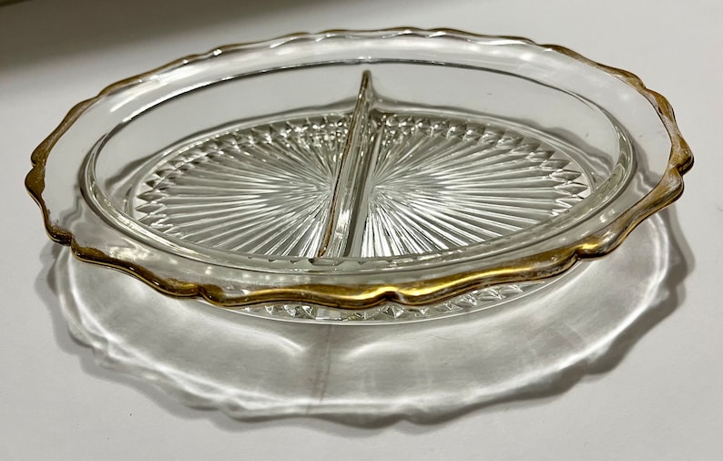 May include: A clear glass divided serving dish with a gold rim. The dish has a scalloped edge and a raised center divider.