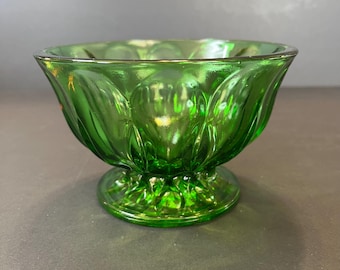 May include: A green glass bowl with a pedestal base. The bowl has a scalloped design around the rim and a textured pattern on the exterior. The glass is a vibrant green color, and the bowl appears to be vintage.